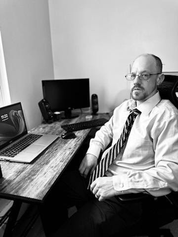 Todd Homer, founder of The AI Geeks, seated at a desk with a laptop.